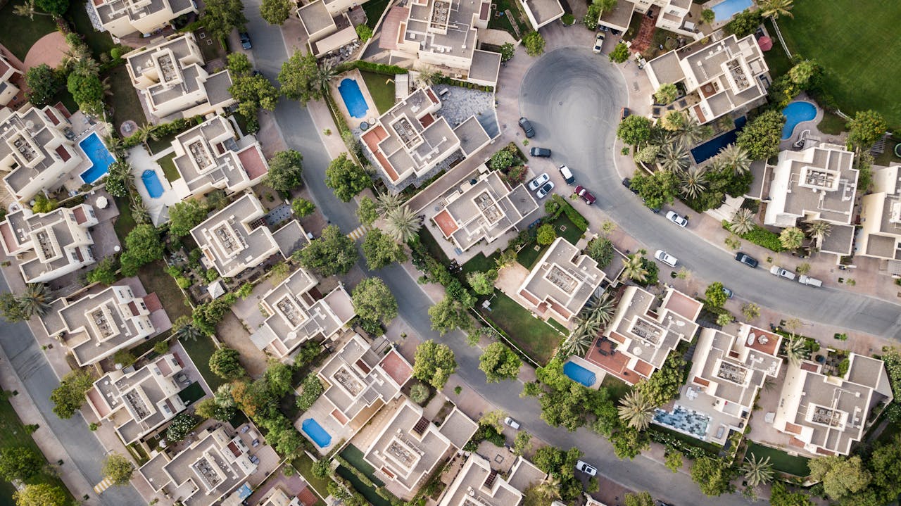 who-we-are Explore a stunning aerial view of a residential area in Dubai with lush greenery and swimming pools.